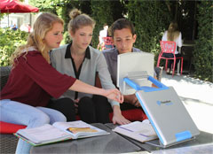 Students in an outdoor courtyard using the TOPAZ PHD portable video magnifier to study