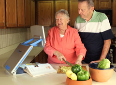 Woman and man making a salad while using the TOPAZ PHD to magnify a recipe in a cookbook