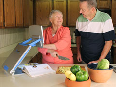 Woman and man preparing a meal while using the TOPAZ PHD to magnify a recipe in a cookbook